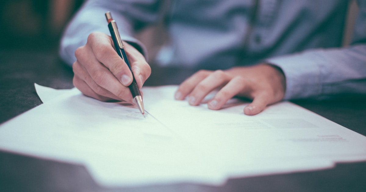 Person signing business documents at a desk